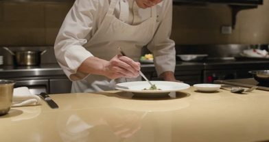 AI-generated frame of a chef plating a dish while the camera orbits the counter in warm restaurant light
