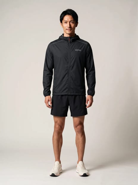 On-model product photo: black jacket and running shoes on studio grey