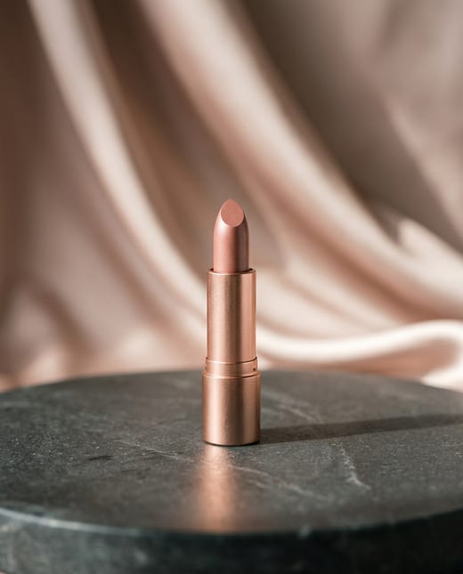 Magazine beauty ad: a rose-gold lipstick on a stone pedestal