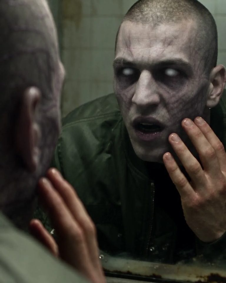 A man staring at his zombie reflection in a bathroom mirror
